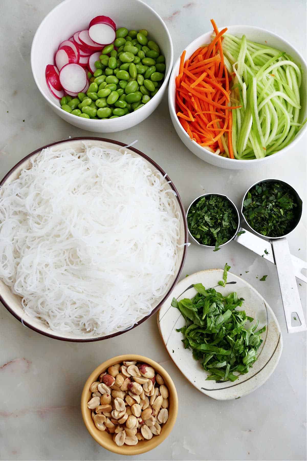 rice noodles, julienned vegetables, herbs, peanuts, and dressing ingredients on a counter