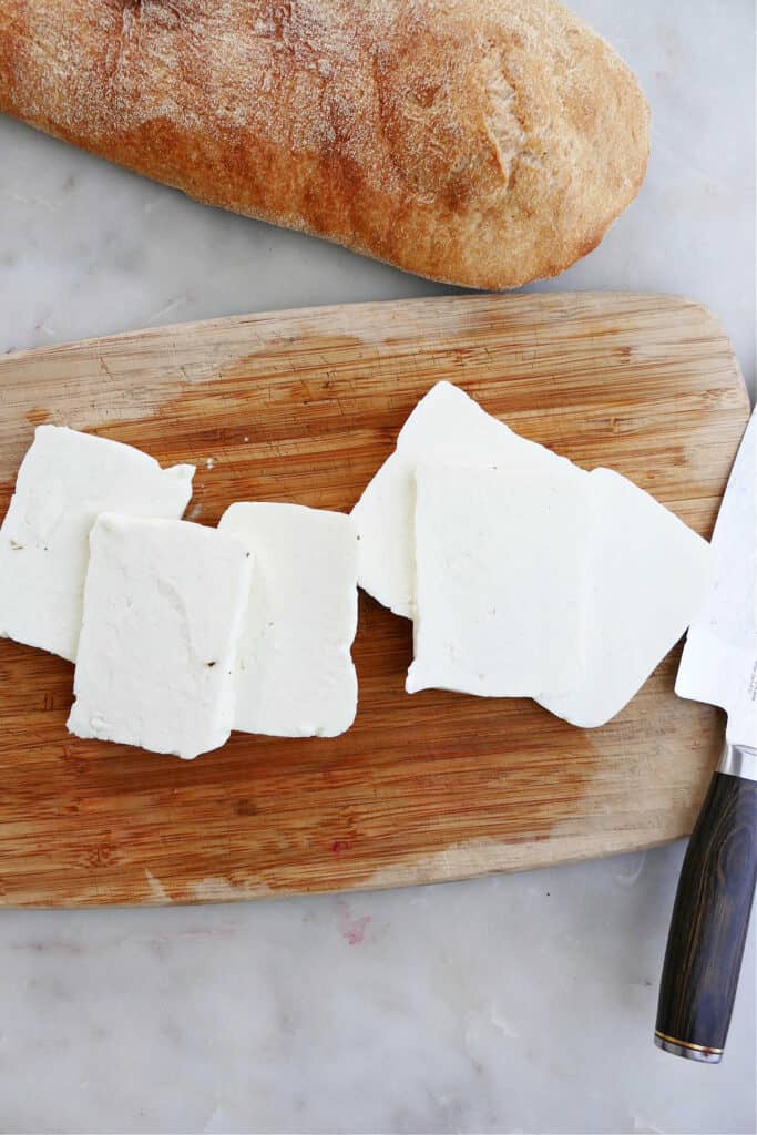 halloumi sliced into pieces on a cutting board next to a loaf of ciabatta