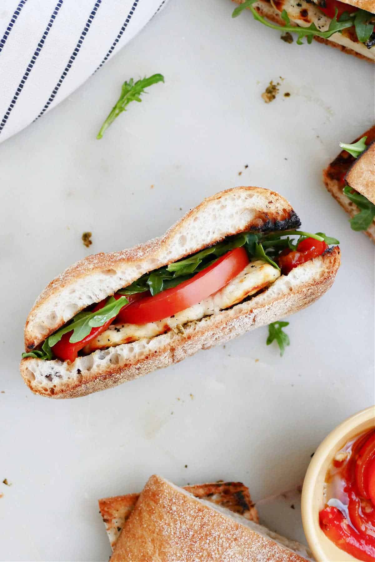 halloumi sandwich with tomato and veggies on its side on a counter