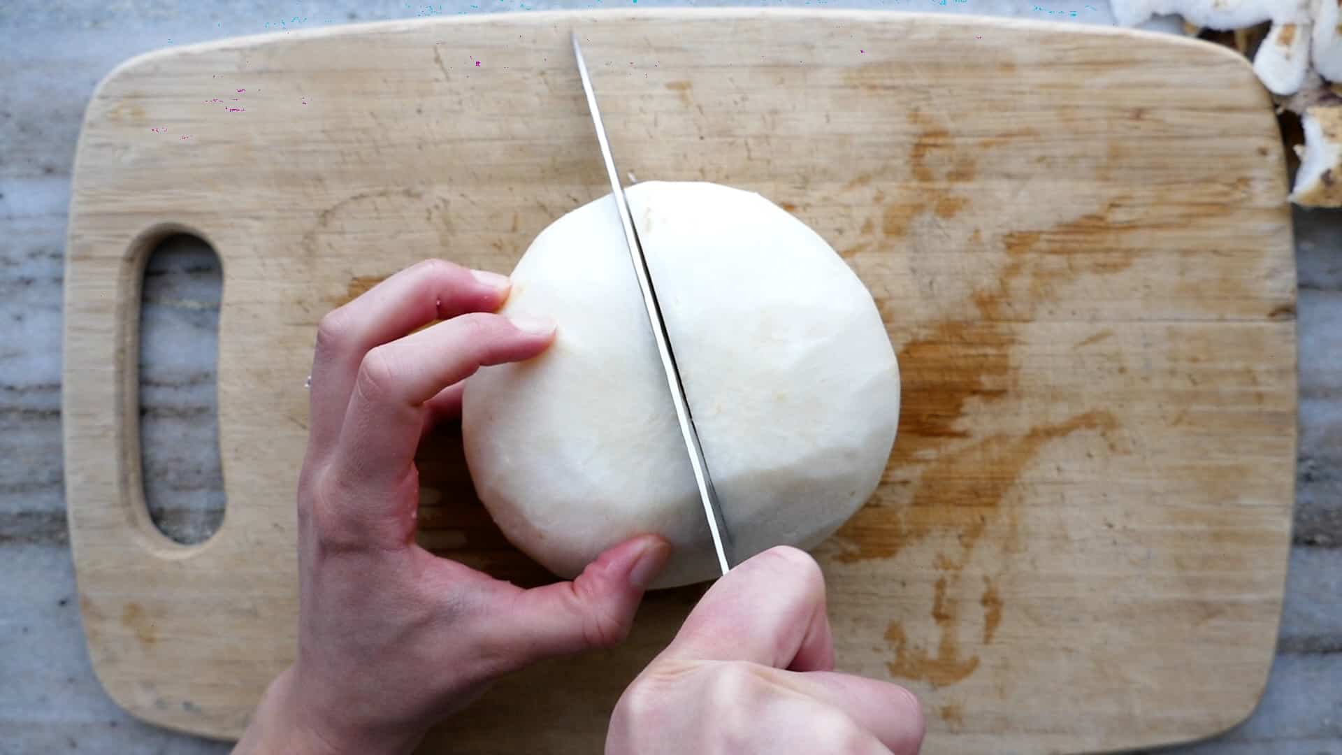 woman cutting a peeled jicama in half with a chef's knife