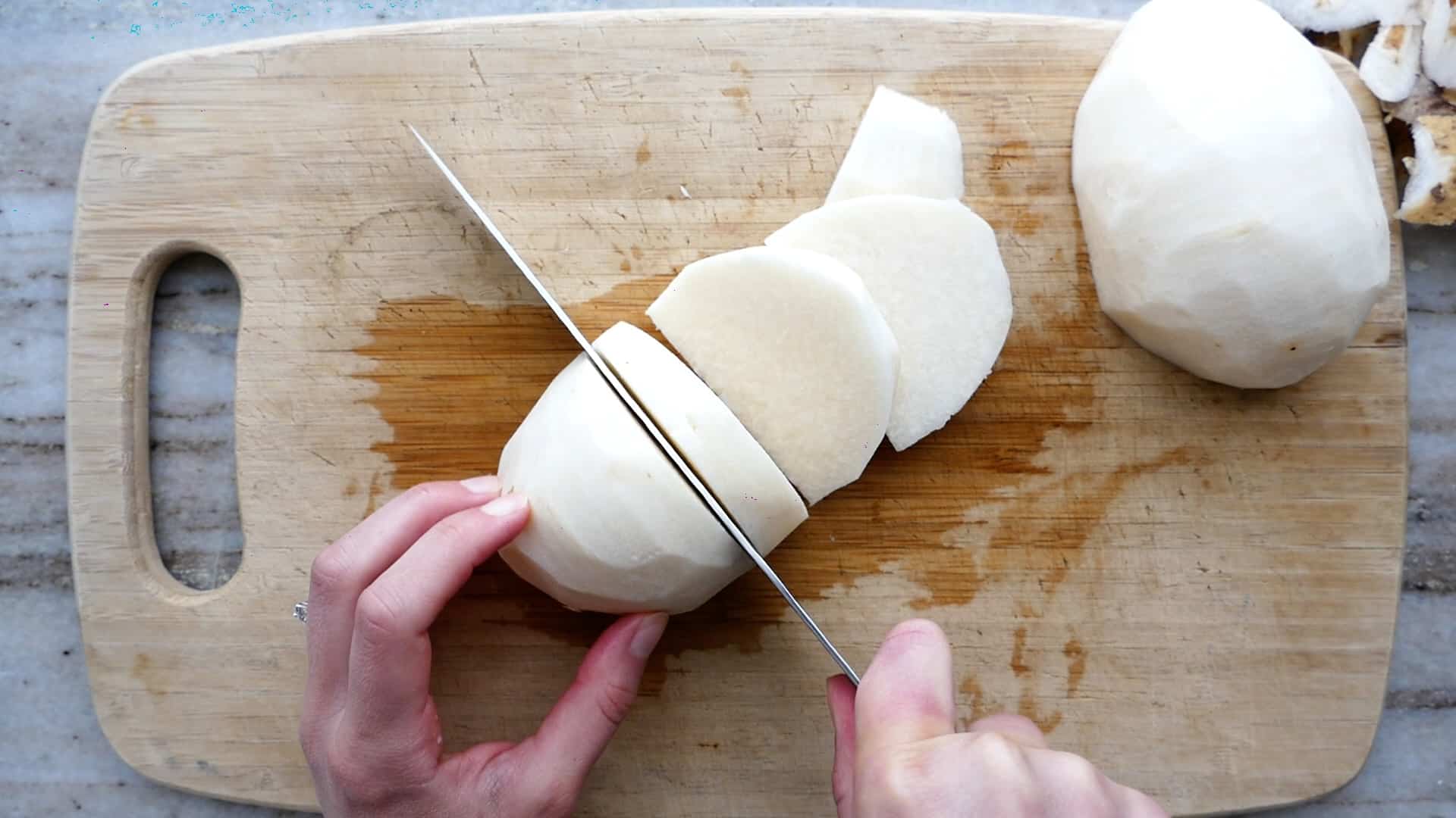 woman cutting jicama into half moon pieces over a cutting board