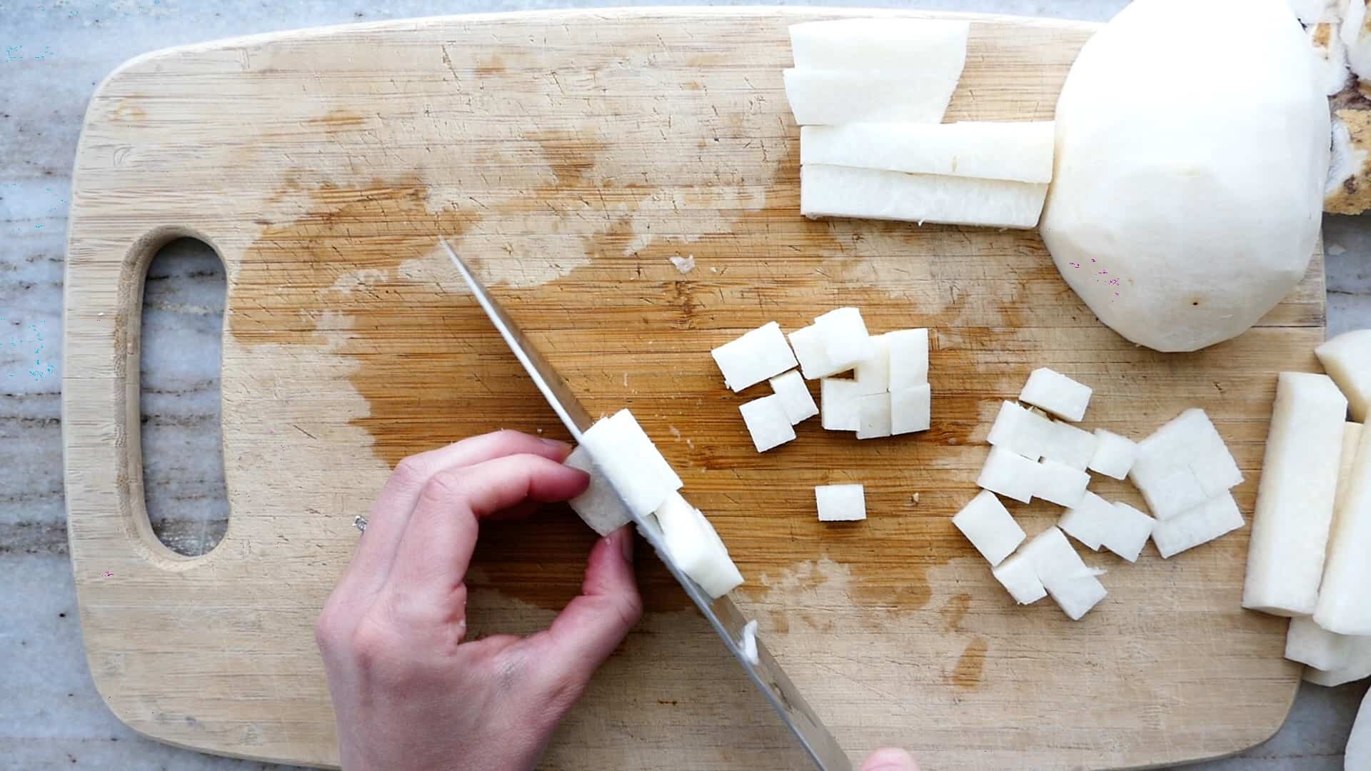 woman cutting jicama into cubes over a bamboo cutting board