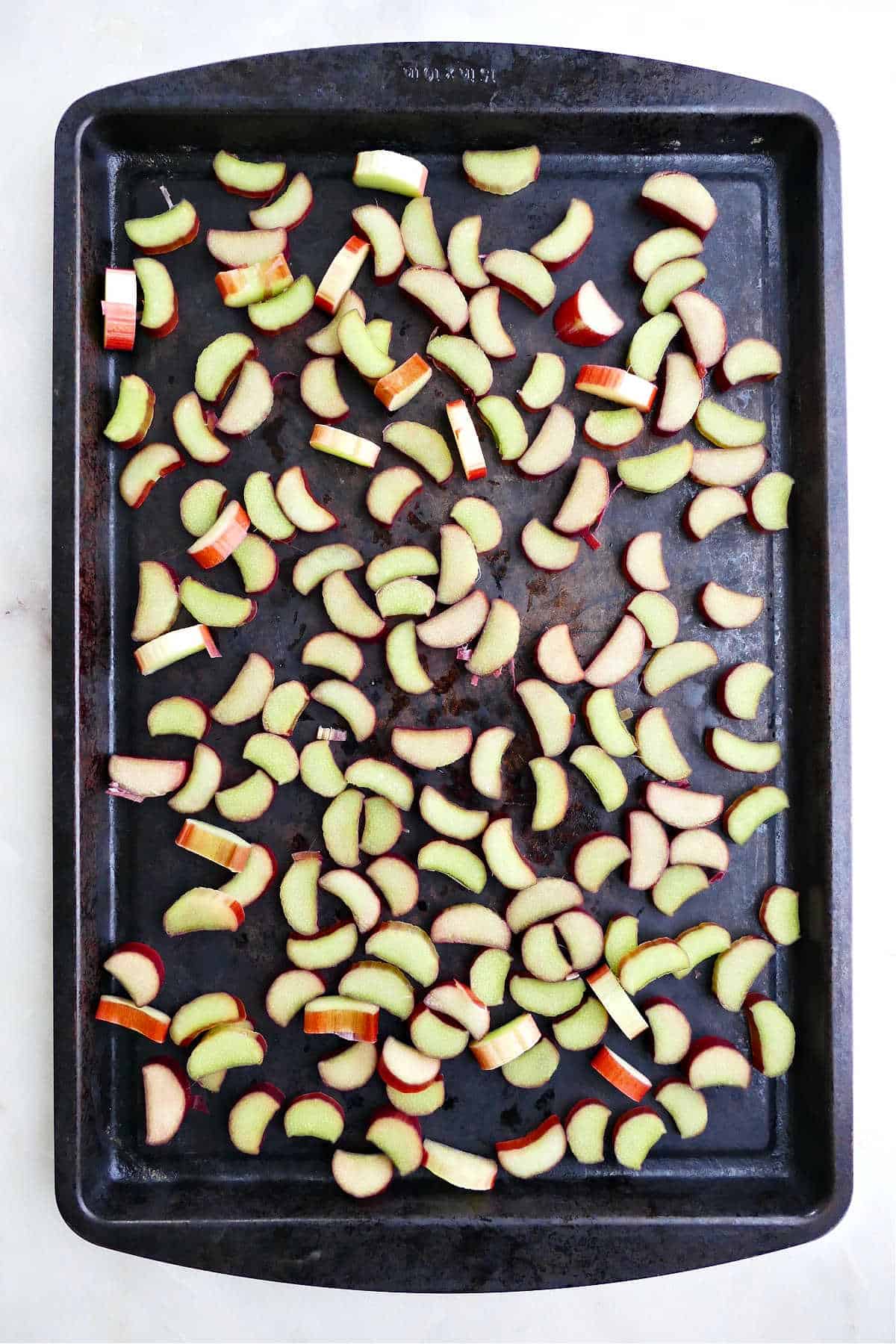 sliced rhubarb spread out in a single layer on a baking sheet for freezing