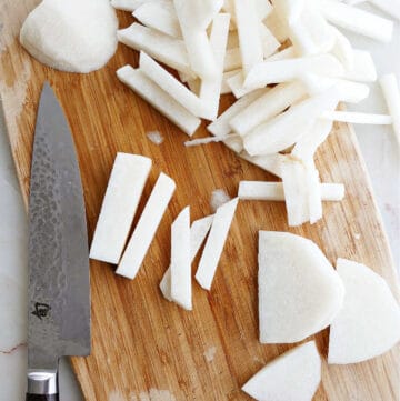 cutting board with jicama sliced into fries next to a chef's knife