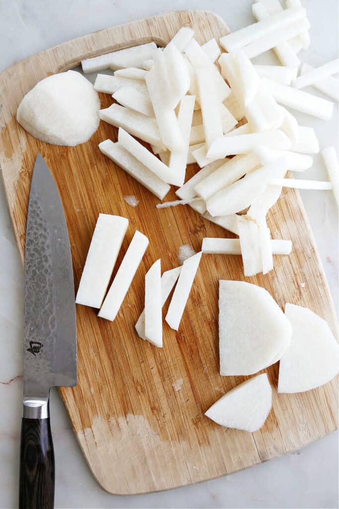 cutting board with jicama sliced into fries next to a chef's knife