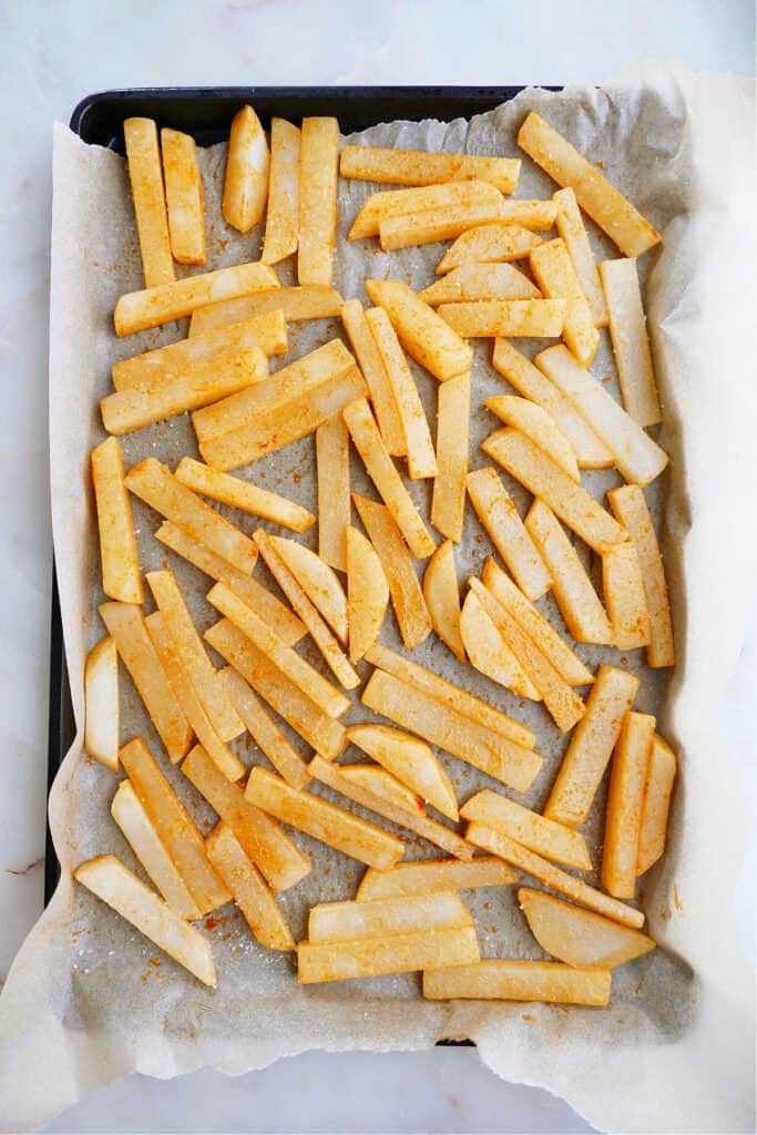jicama fries tossed in paprika spread out on a lined baking sheet