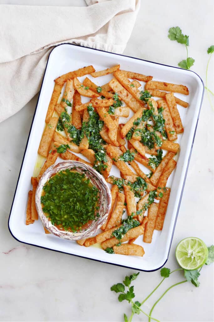 jicama fries drizzled with cilantro lime dressing on a serving tray on a counter