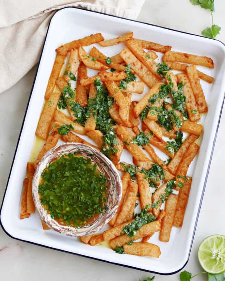 square image of jicama fries drizzled with cilantro lime dressing on a serving tray on a counter