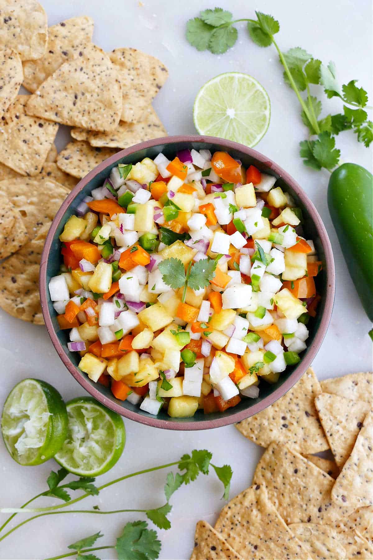 pineapple jicama salsa in a serving bowl surrounded by chips, lime, and cilantro