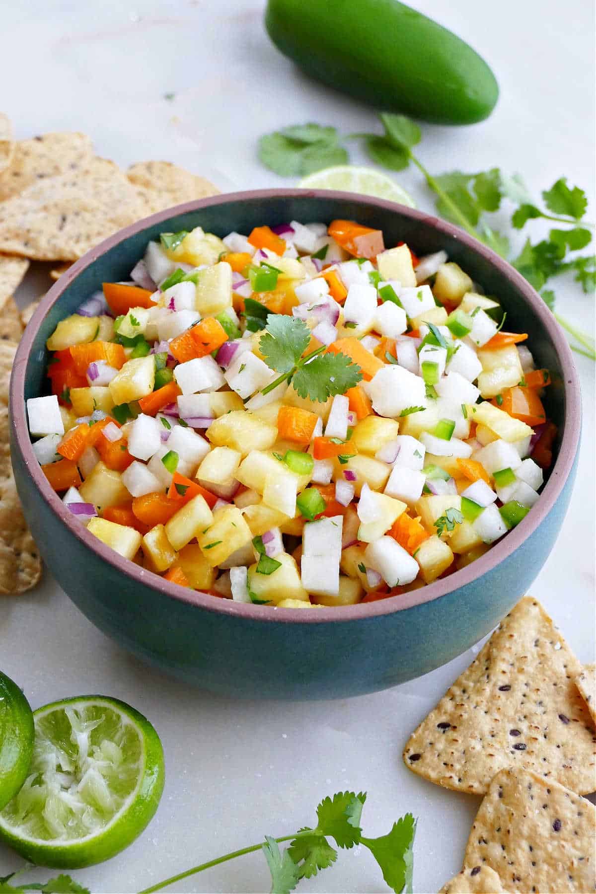 pineapple jicama salsa in a serving bowl surrounded by chips, lime, and cilantro