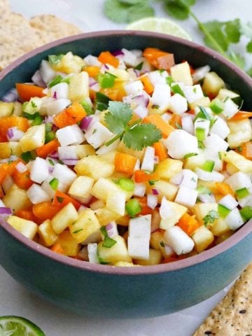 pineapple jicama salsa in a serving bowl surrounded by chips, lime, and cilantro