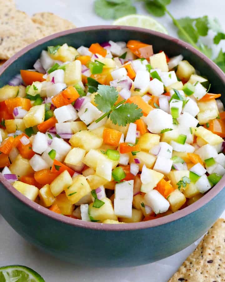 pineapple jicama salsa in a serving bowl surrounded by chips, lime, and cilantro