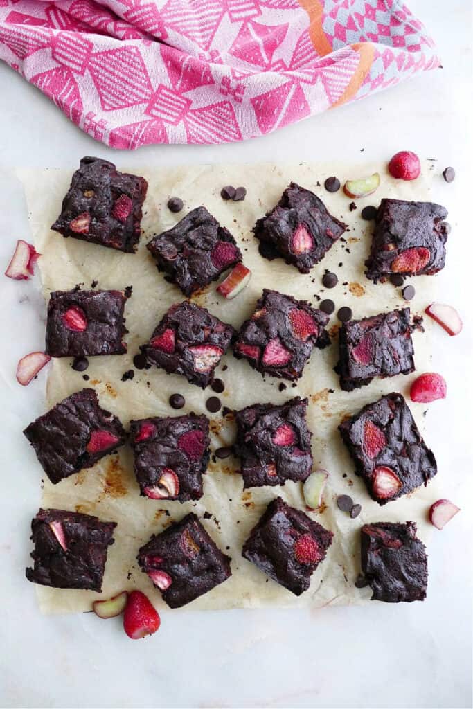 sixteen strawberry rhubarb brownies on a piece of parchment next to a pink napkin