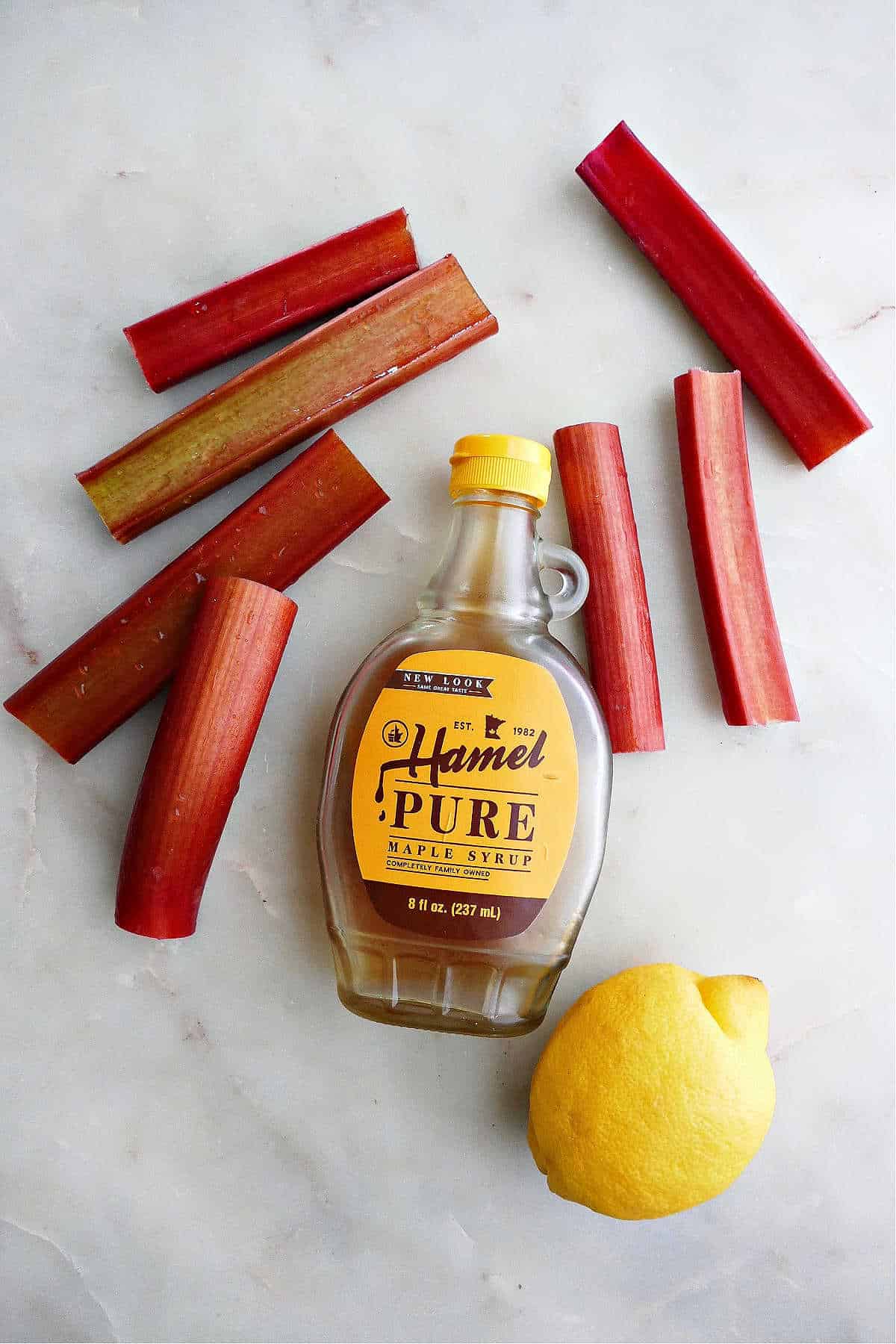stalks of rhubarb next to a maple syrup container and a lemon on a counter