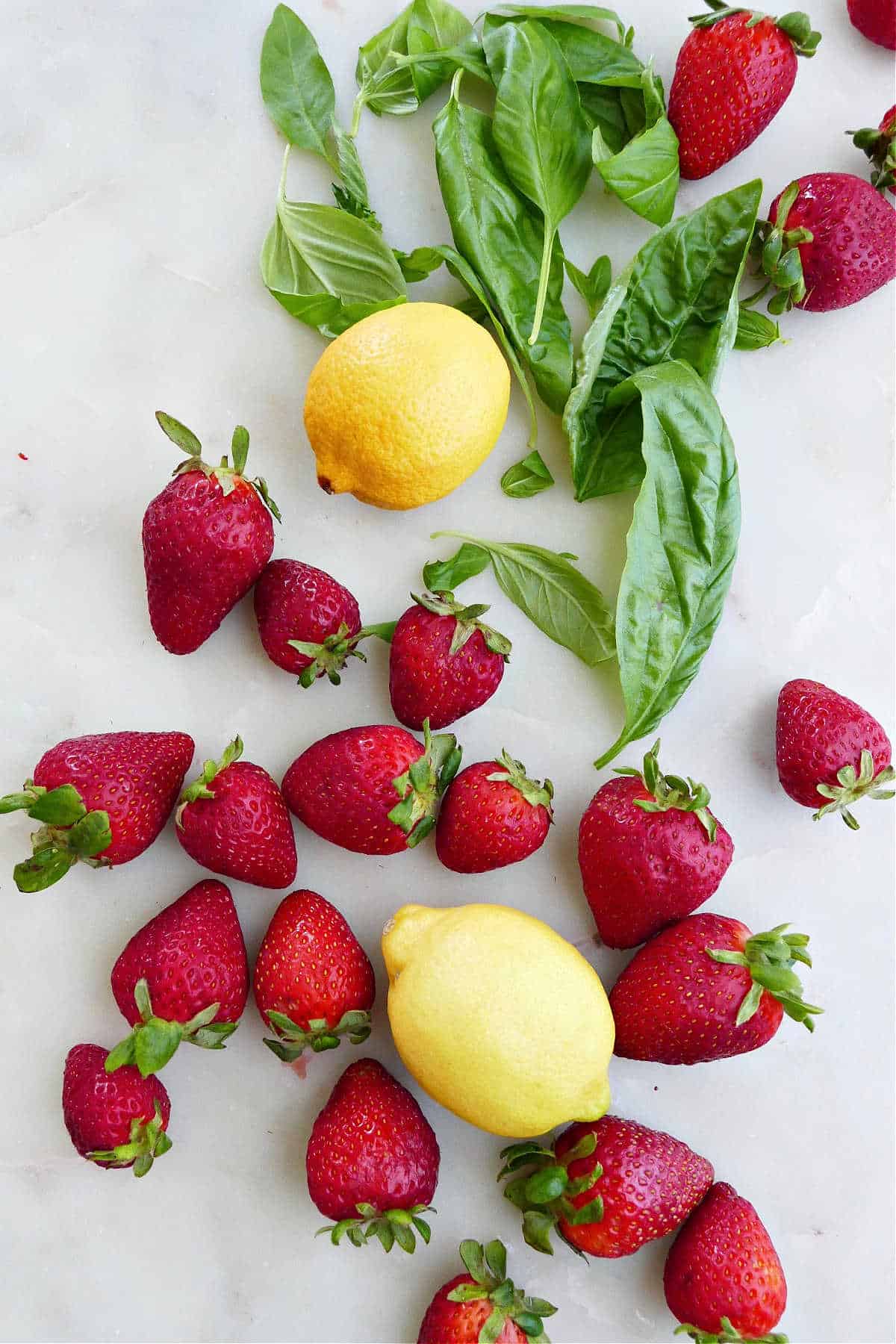 basil leaves, strawberries, and lemons spread out on a marble counter