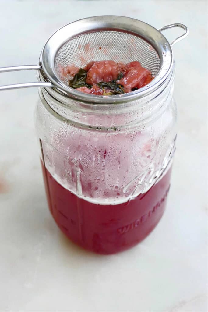 strawberry basil simple syrup poured through a mesh sieve into a mason jar