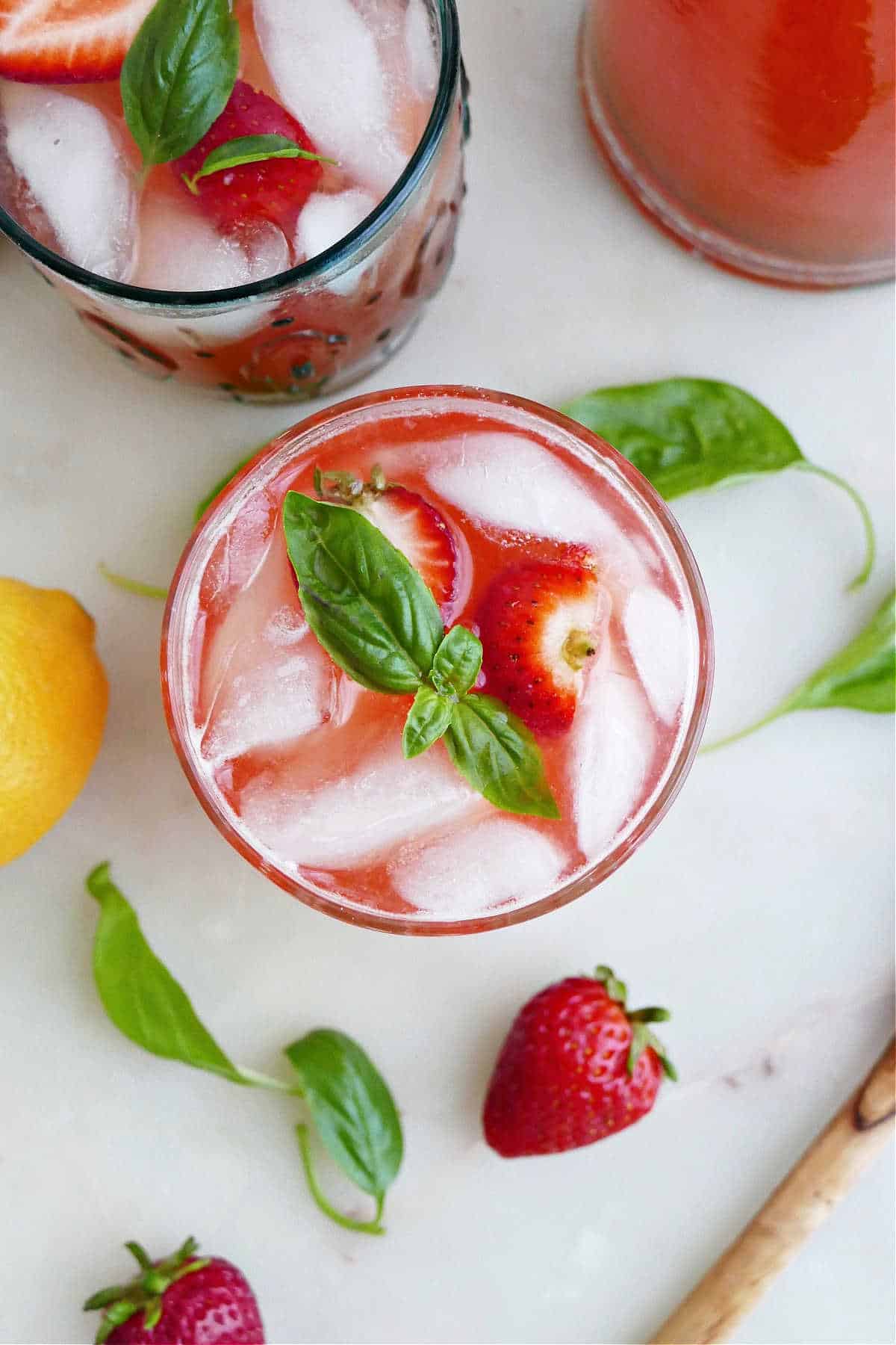 strawberry basil lemonade topped with basil leaves on a counter next to ingredients