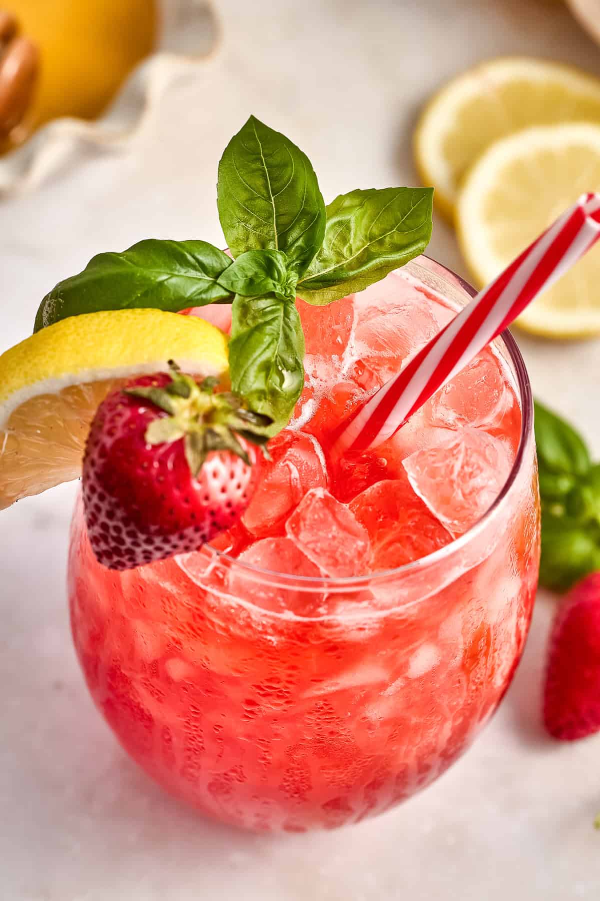 Strawberry basil lemonade over ice with red and white straw and garnishes.