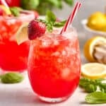 Glass of strawberry basil lemonade with red and white straw and strawberry, basil, and lemon garnish.