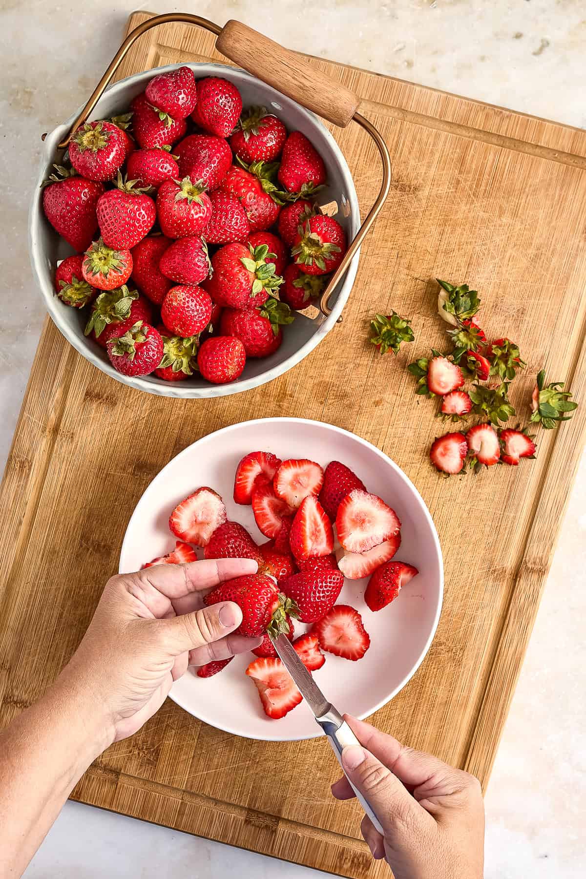Woman removing the stems from strawberries with a knife over a bowl.