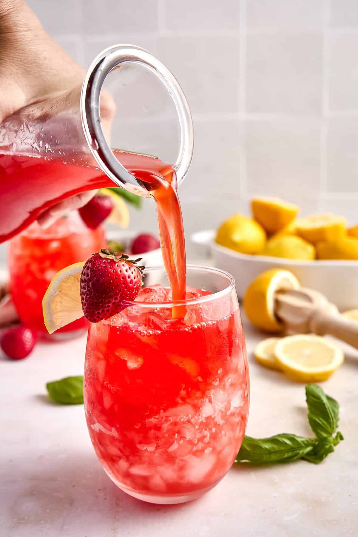 Woman pouring a pitcher of homemade strawberry basil lemonade into a glass with ice.