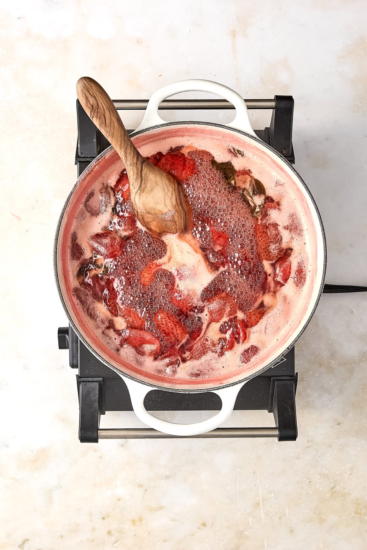 Strawberry basil simple syrup cooked down in a large pot with a spoon.