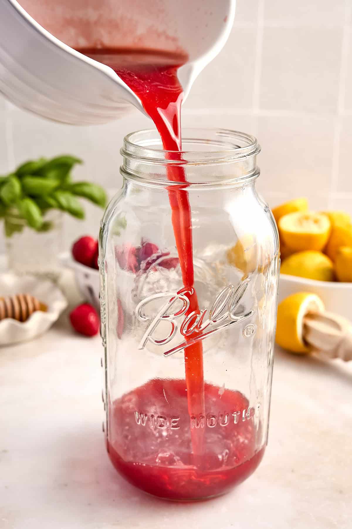 Woman pouring a pitcher of strawberry basil simple syrup into a glass jar.