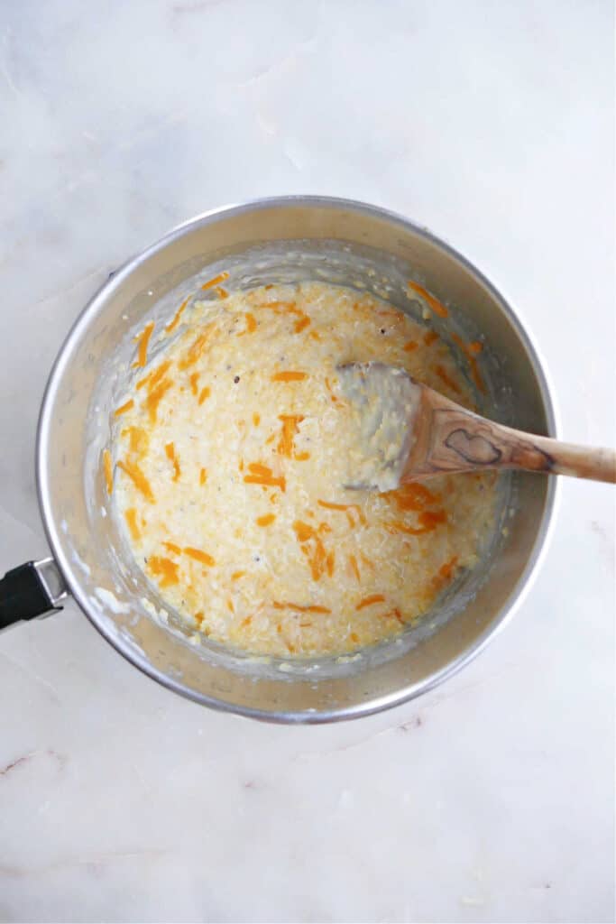 cheesy grits cooking in a saucepan with a wooden spoon on a counter