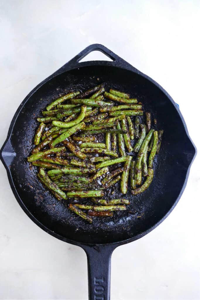 blackened green beans cooking in a cast iron skillet on a counter