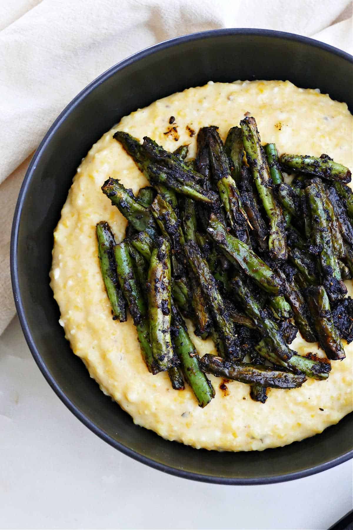 blackened green beans sitting on top of cheesy grits in a serving bowl