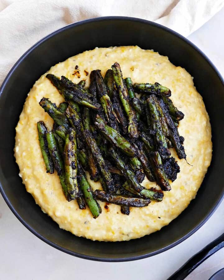 blackened green beans sitting on top of cheesy grits in a serving bowl