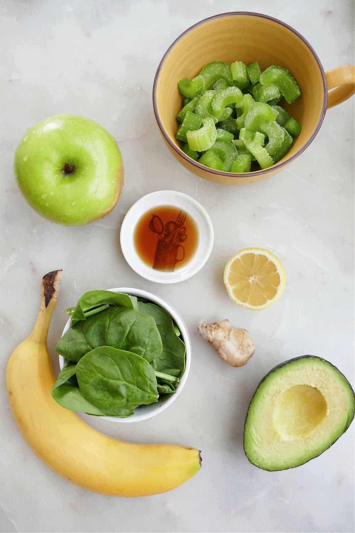 chopped celery, apple, banana, spinach, avocado, ginger, lemon, and vanilla on a counter