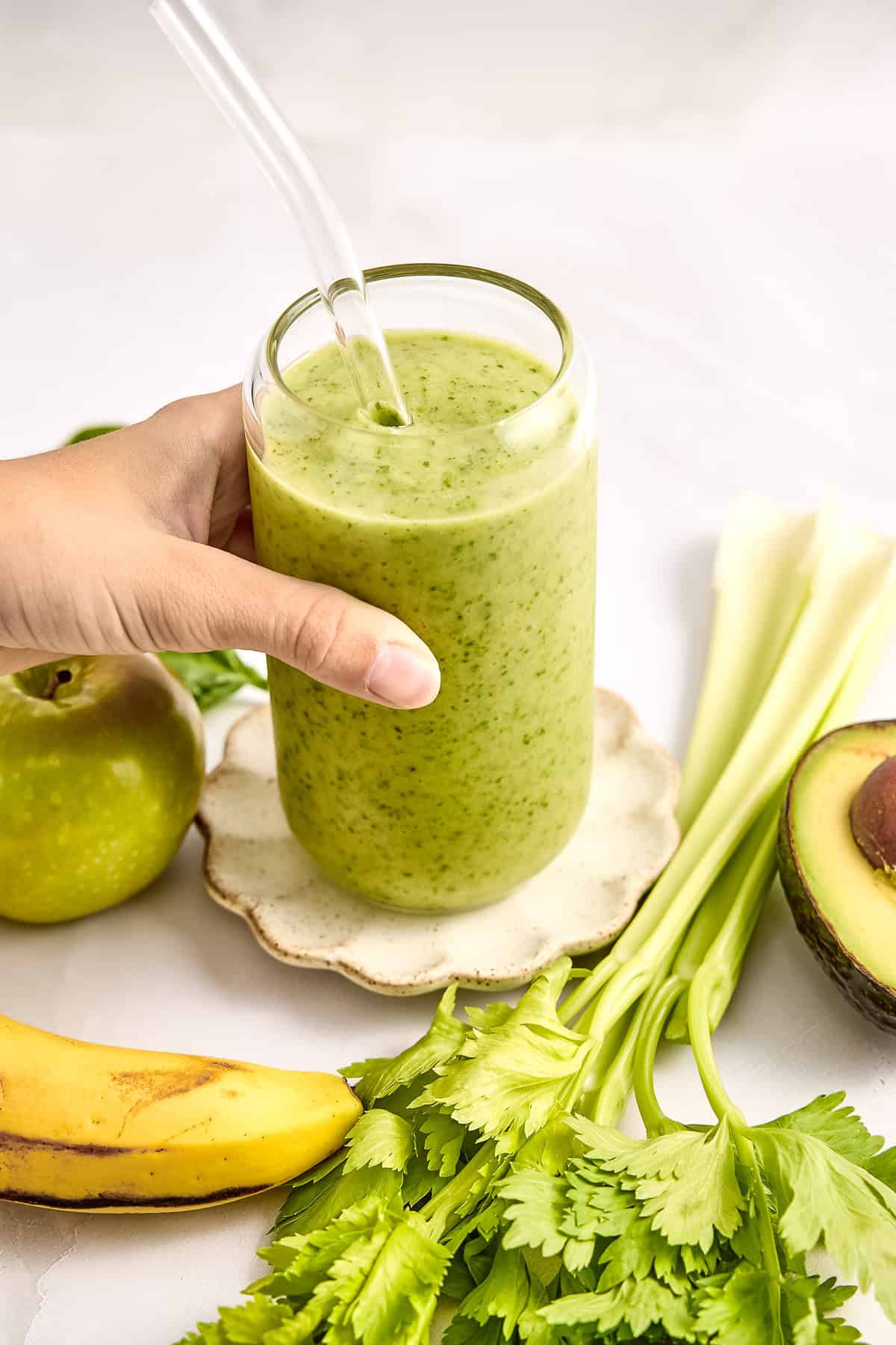 Woman putting celery smoothie on a small plate next to ingredients.