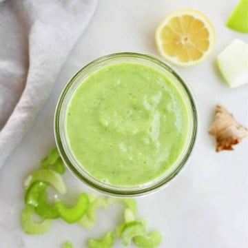 green celery apple smoothie in a glass jar on a counter next to ingredients