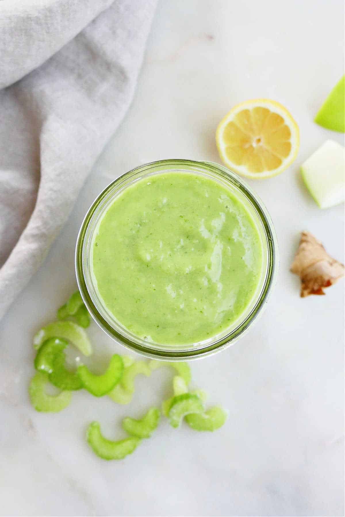 green celery apple smoothie in a glass jar on a counter next to ingredients