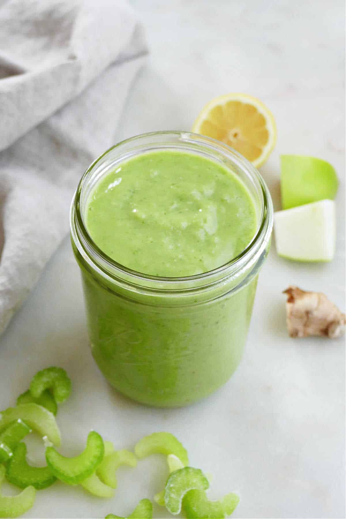 green smoothie made from celery in glass jar on a counter next to ingredients