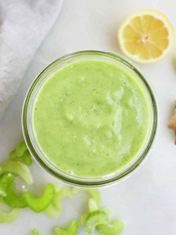 green celery apple smoothie in a glass jar on a counter next to ingredients
