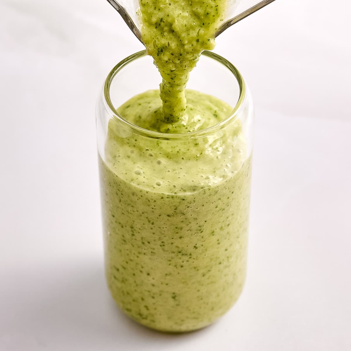 Green smoothie being poured into a glass.