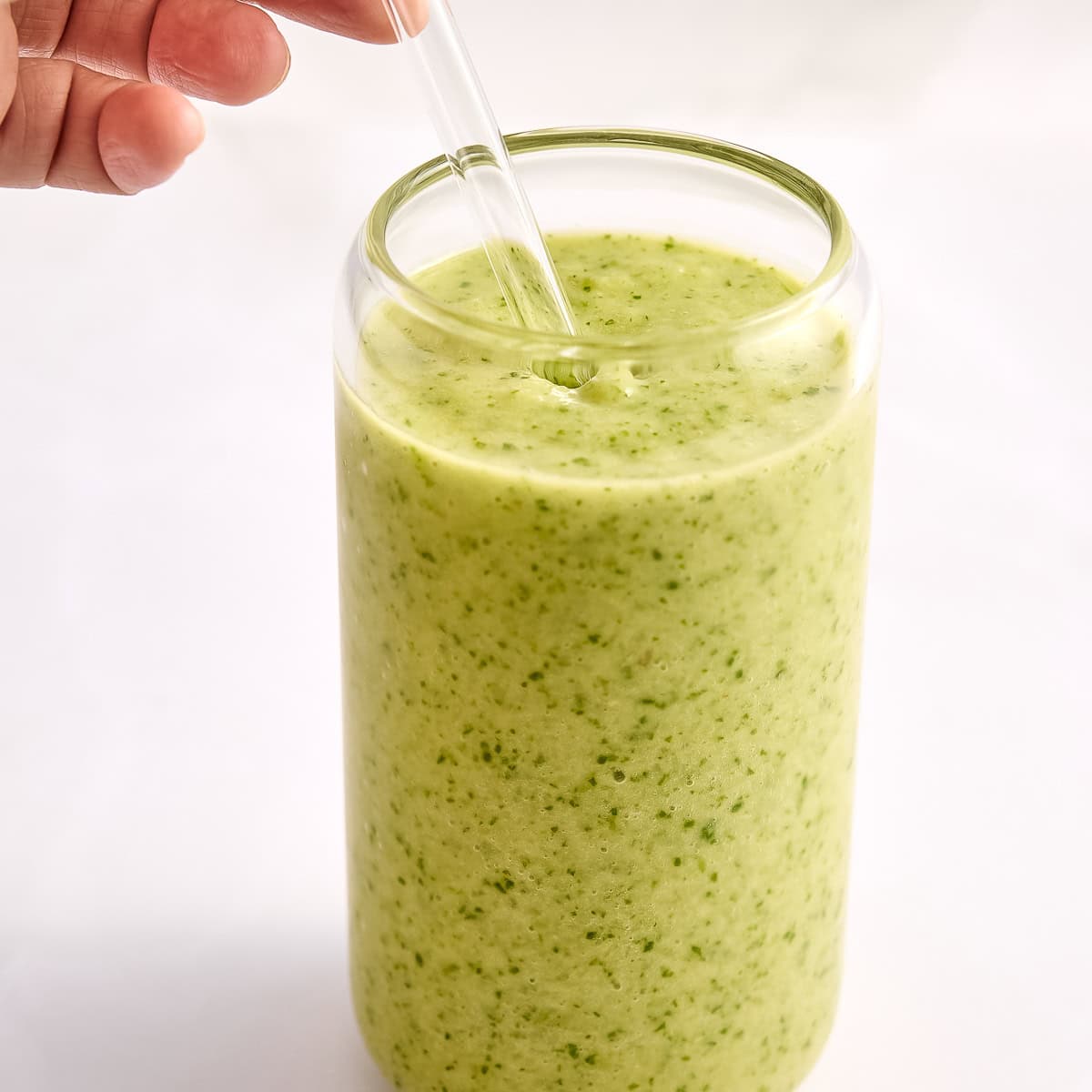 Woman putting a glass straw into a glass of celery smoothie.