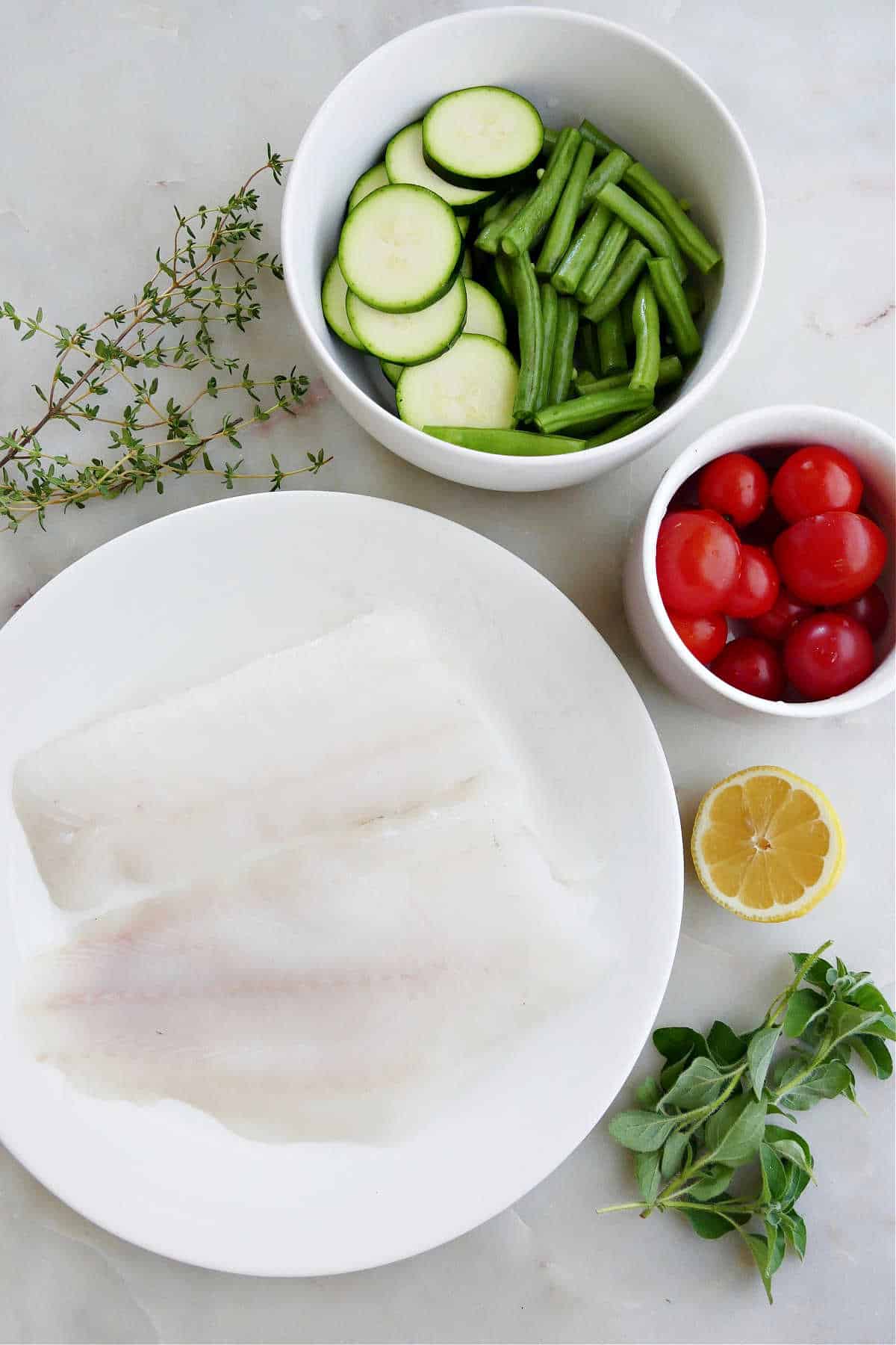 cod fillets, vegetables, lemon, and herbs spread out next to each other on a counter
