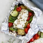 cod foil packet with summer vegetables on a counter next to a napkin