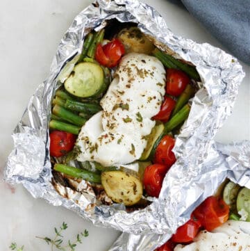 cod foil packet with summer vegetables on a counter next to a napkin