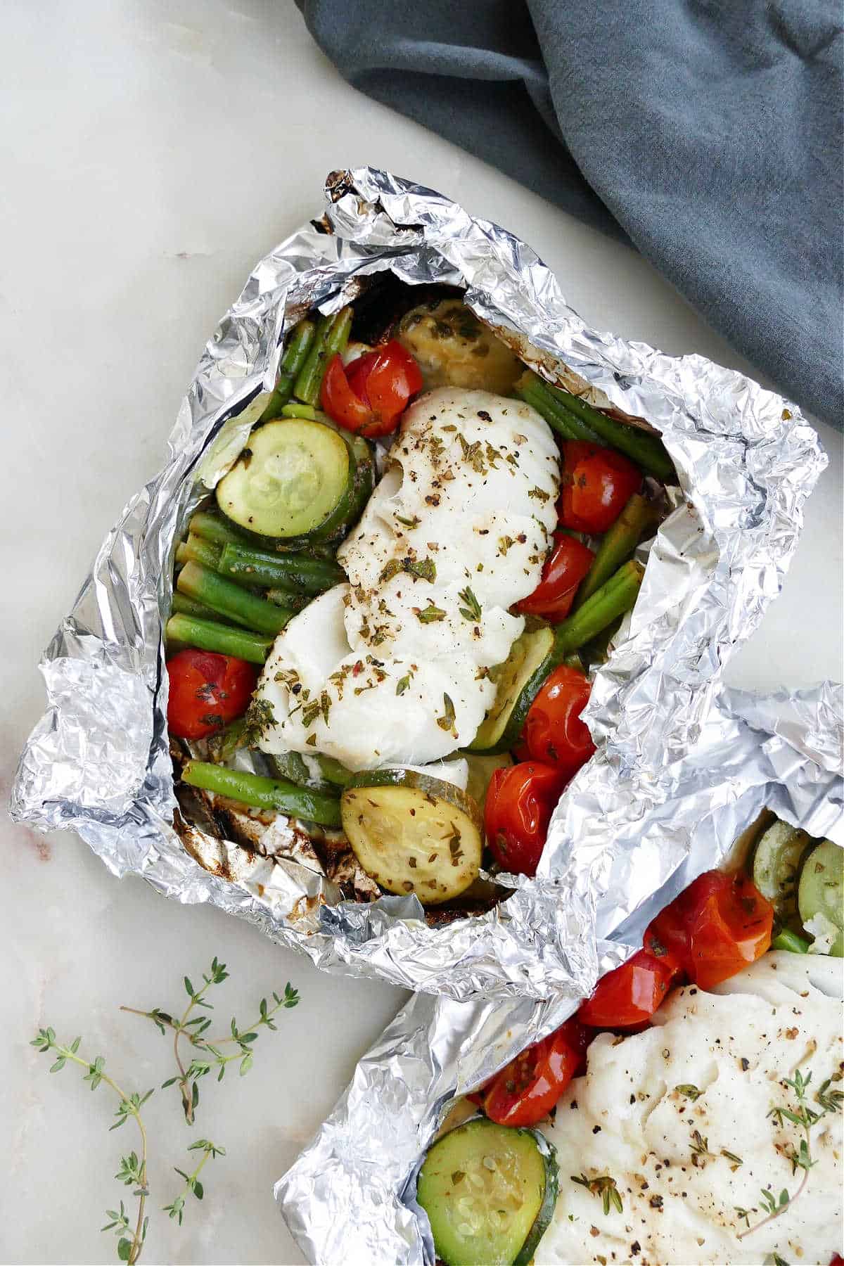 cod foil packet with summer vegetables on a counter next to a napkin