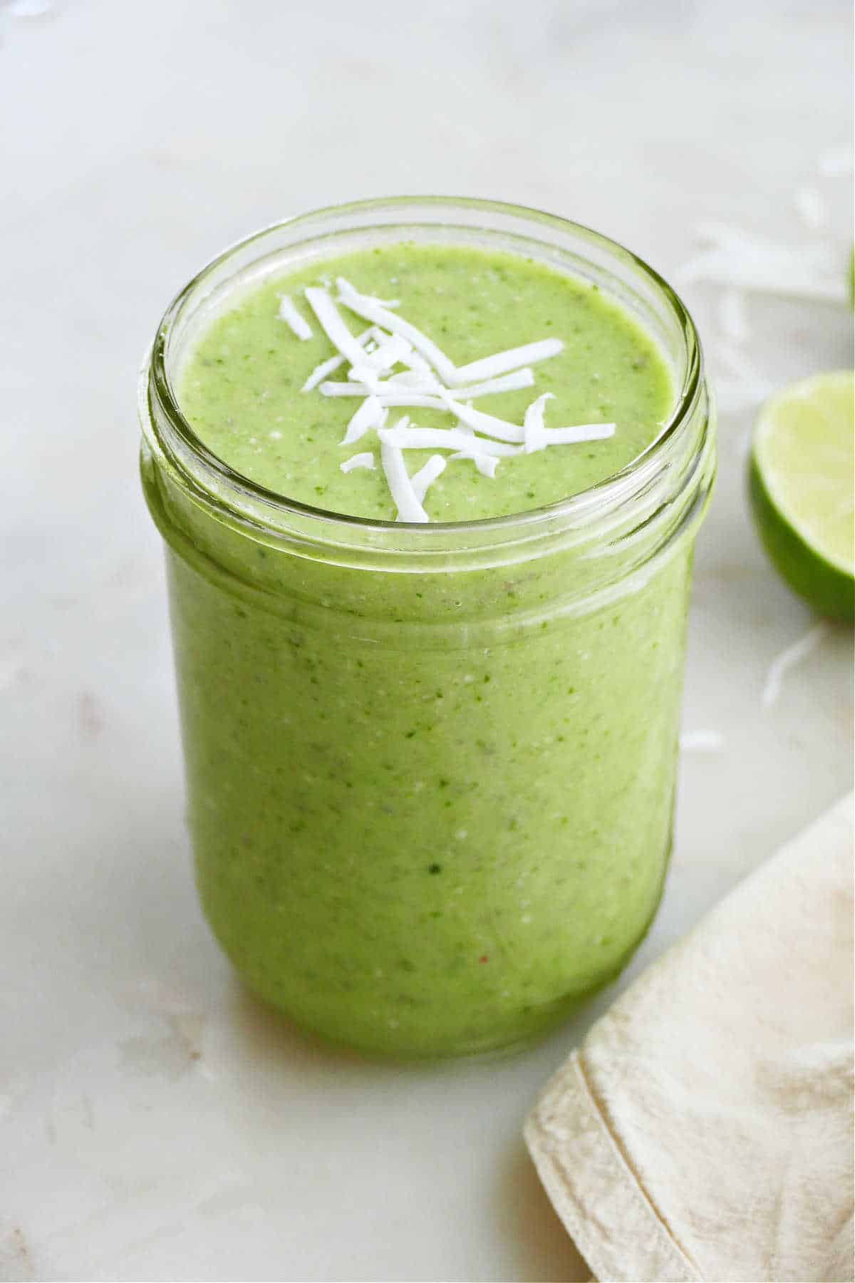 cucumber smoothie topped with shredded coconut flakes in a glass jar on a counter