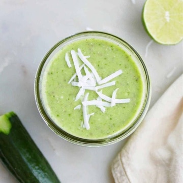 cucumber smoothie topped with shredded coconut flakes on a counter next to ingredients