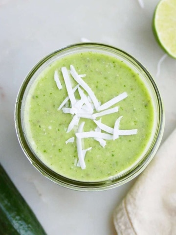 cucumber smoothie topped with shredded coconut flakes on a counter next to ingredients
