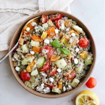Greek lentil salad in a serving bowl next to tomatoes, lemon, and a napkin