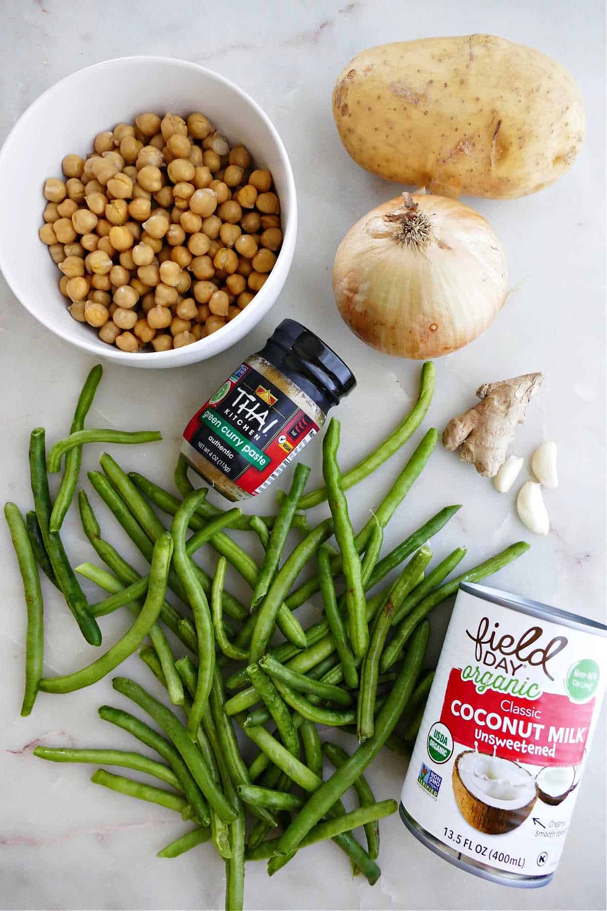 chickpeas, yellow potato, onion, ginger, garlic, green beans, curry paste, and coconut milk on a counter