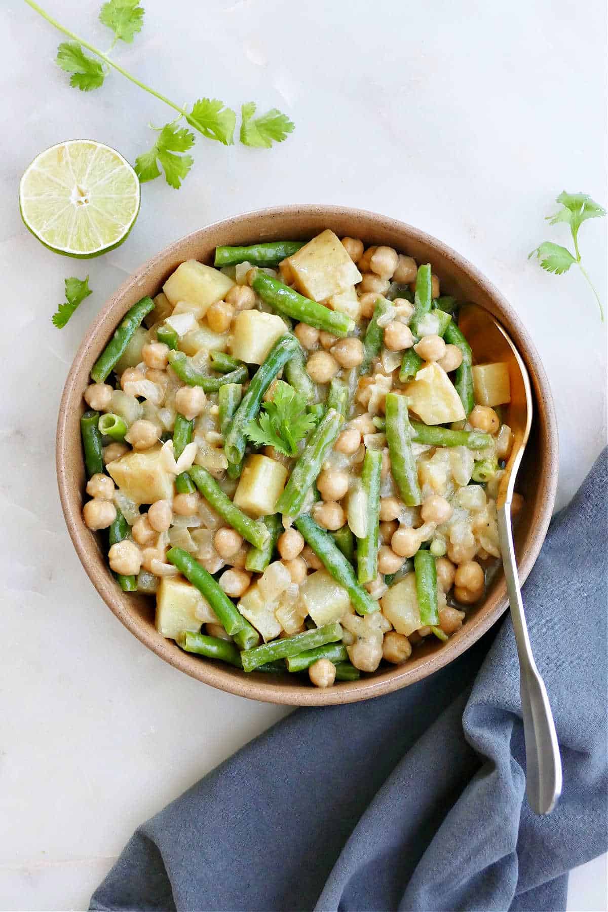 green bean curry in a serving dish next to napkin and toppings on a counter