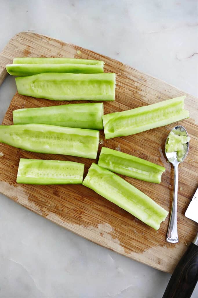 sliced cucumber with seeds being scooped out on a bamboo cutting board